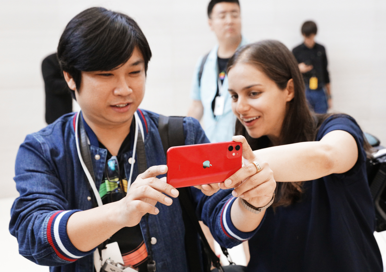 A man holding a red iPhone with a woman standing next to him touching the screen