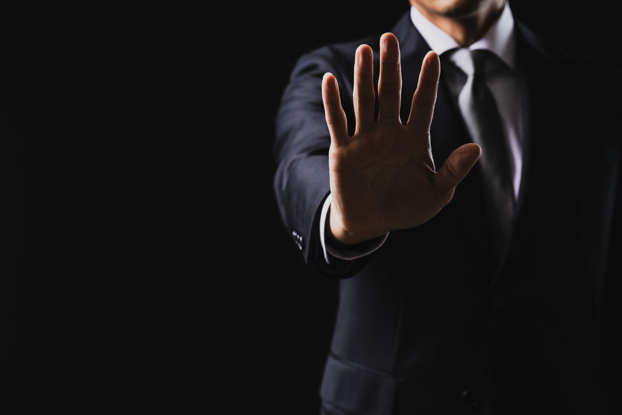 A person in a business suit raising his hand out in front of his body with his fingers outstretched 