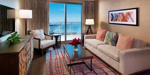 Room with couch, table, dresser, and chair, with window showing beach view.