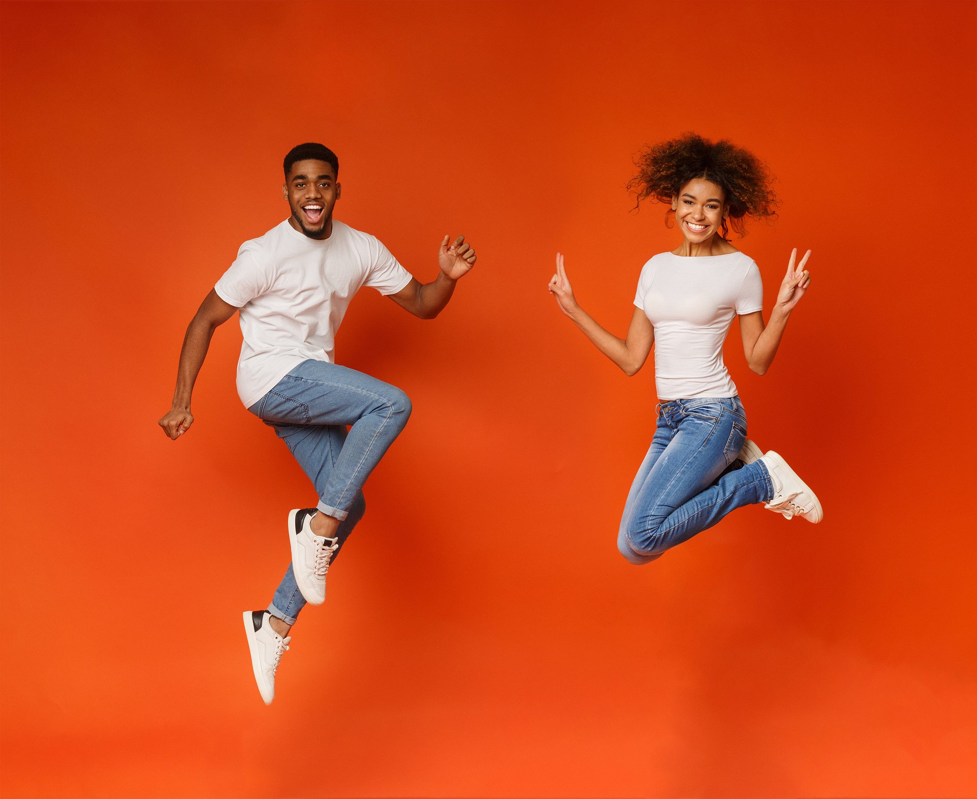 A smiling young man and woman jumping in the air.