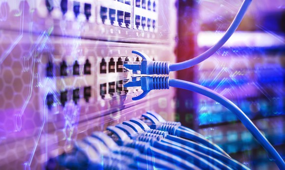 Ethernet cords plugged into the back of a switch on a rack in a data center