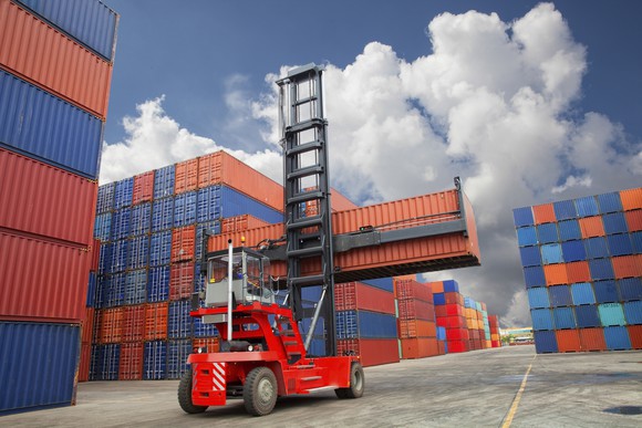 A lift vehicle moves a shipping container in a port.