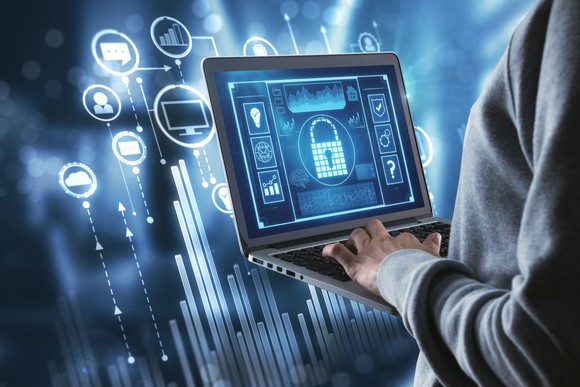 A man holding a laptop with technology-related graphics hovering behind it. 