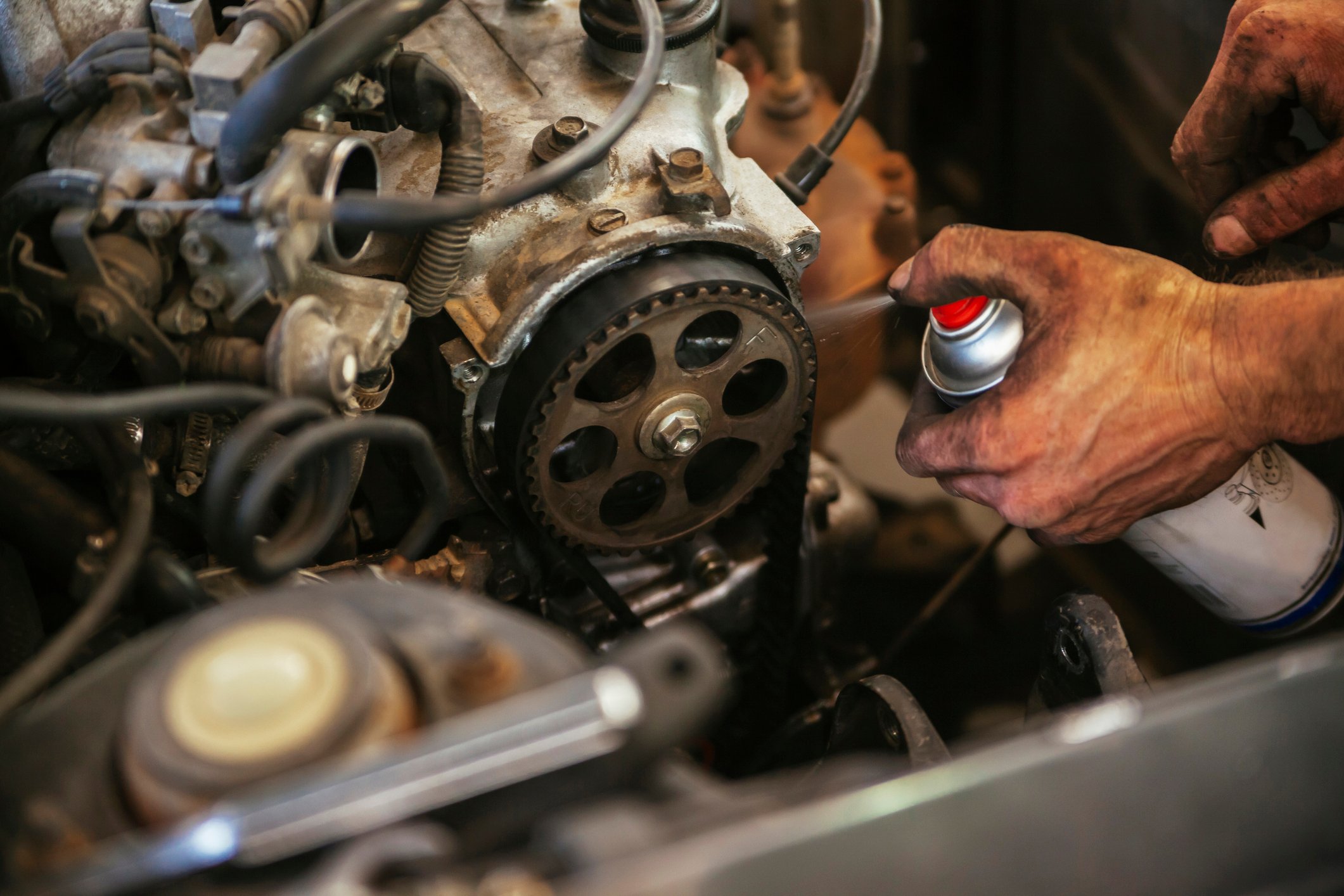 A mechanic sprays lubricant in a car engine.