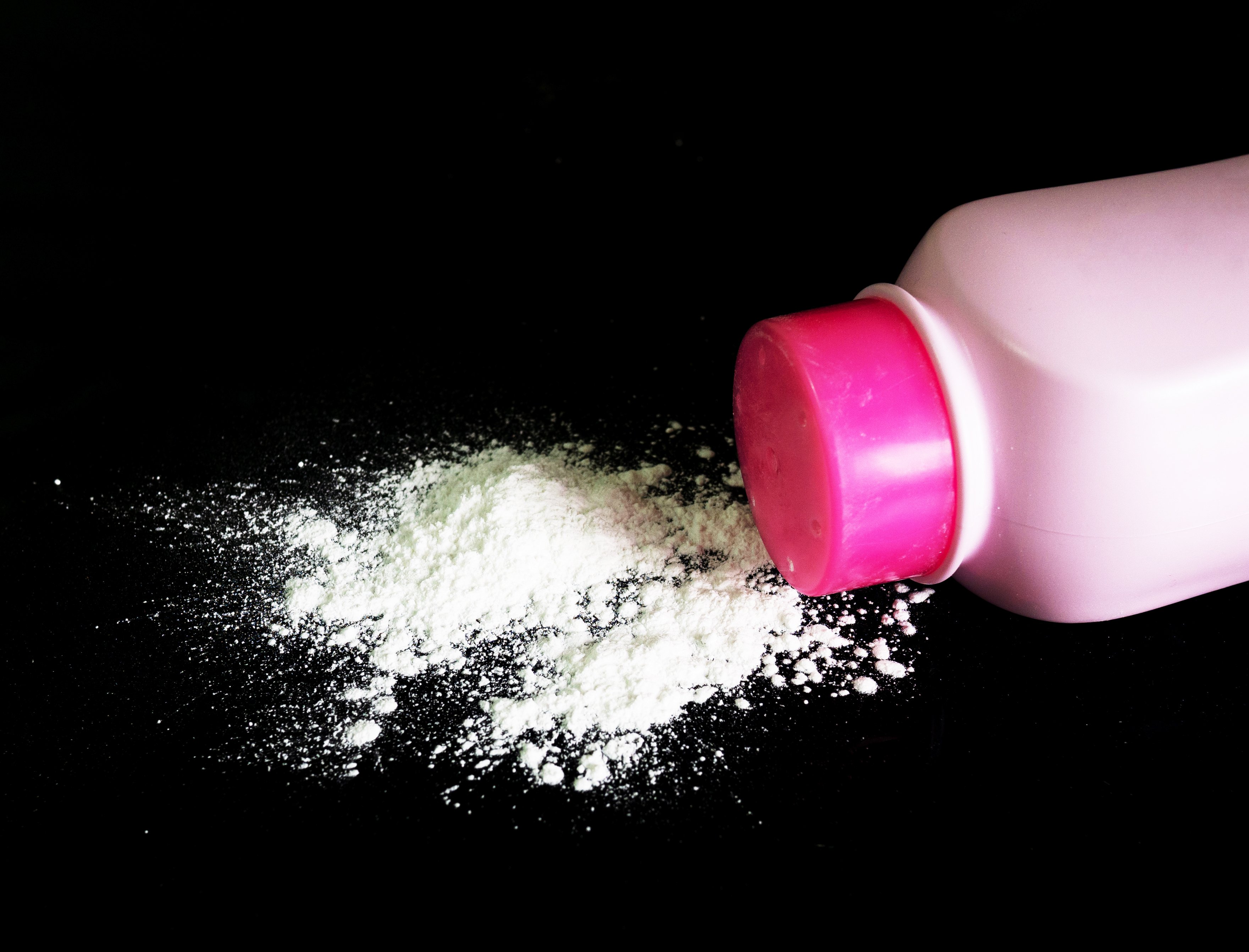 Baby powder on a black surface next to a pink plastic bottle