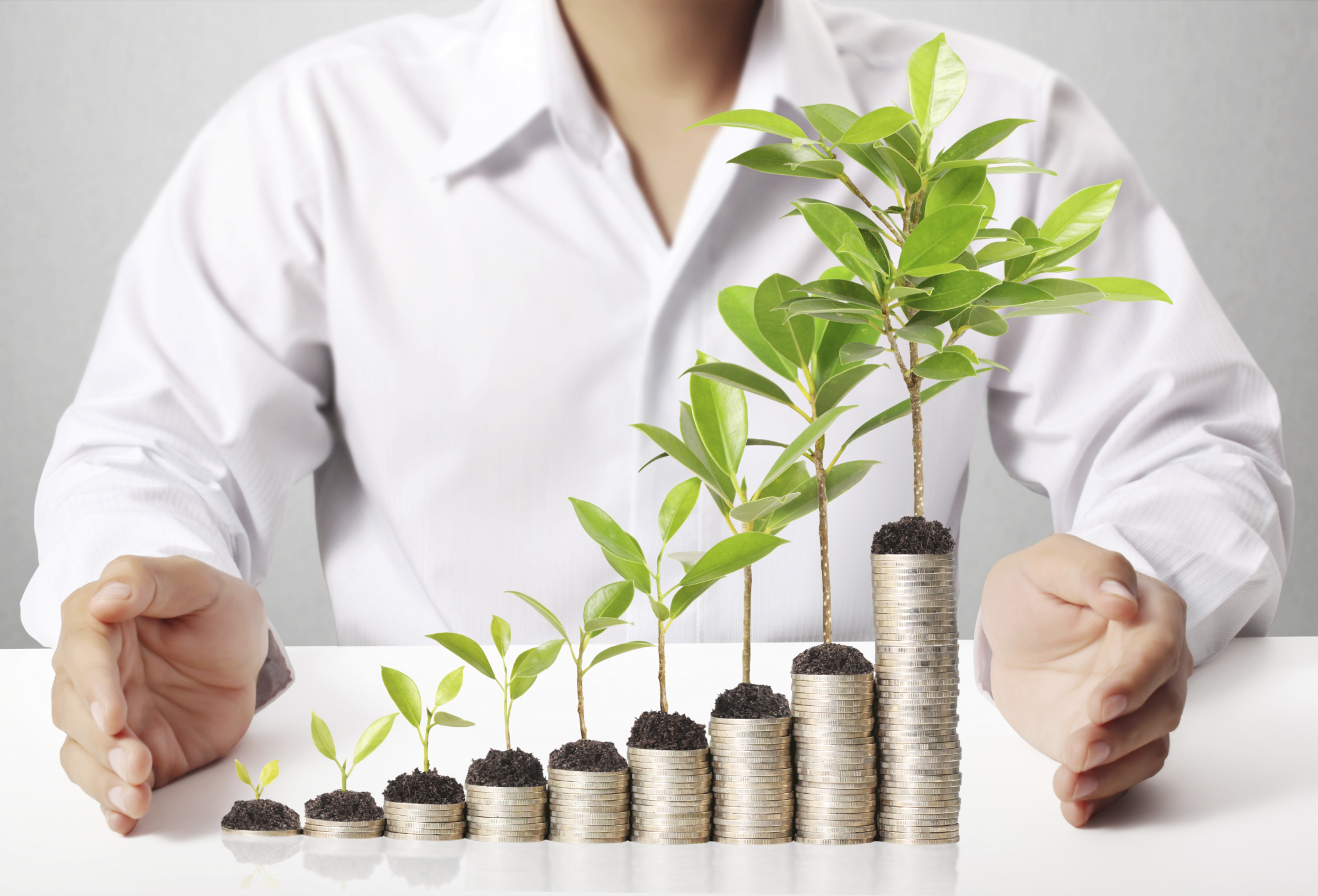 A man standing behind an ascending stack of coins, with progressively larger plants sprouting out of the top of each stack.