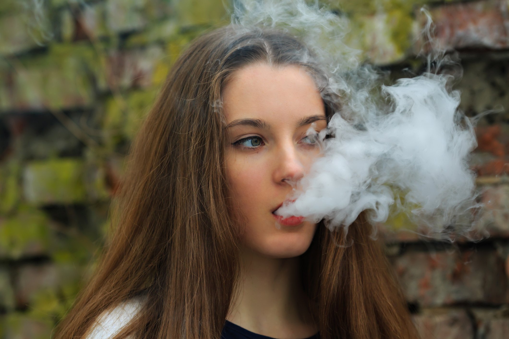 A young woman blowing vapor out of her mouth.