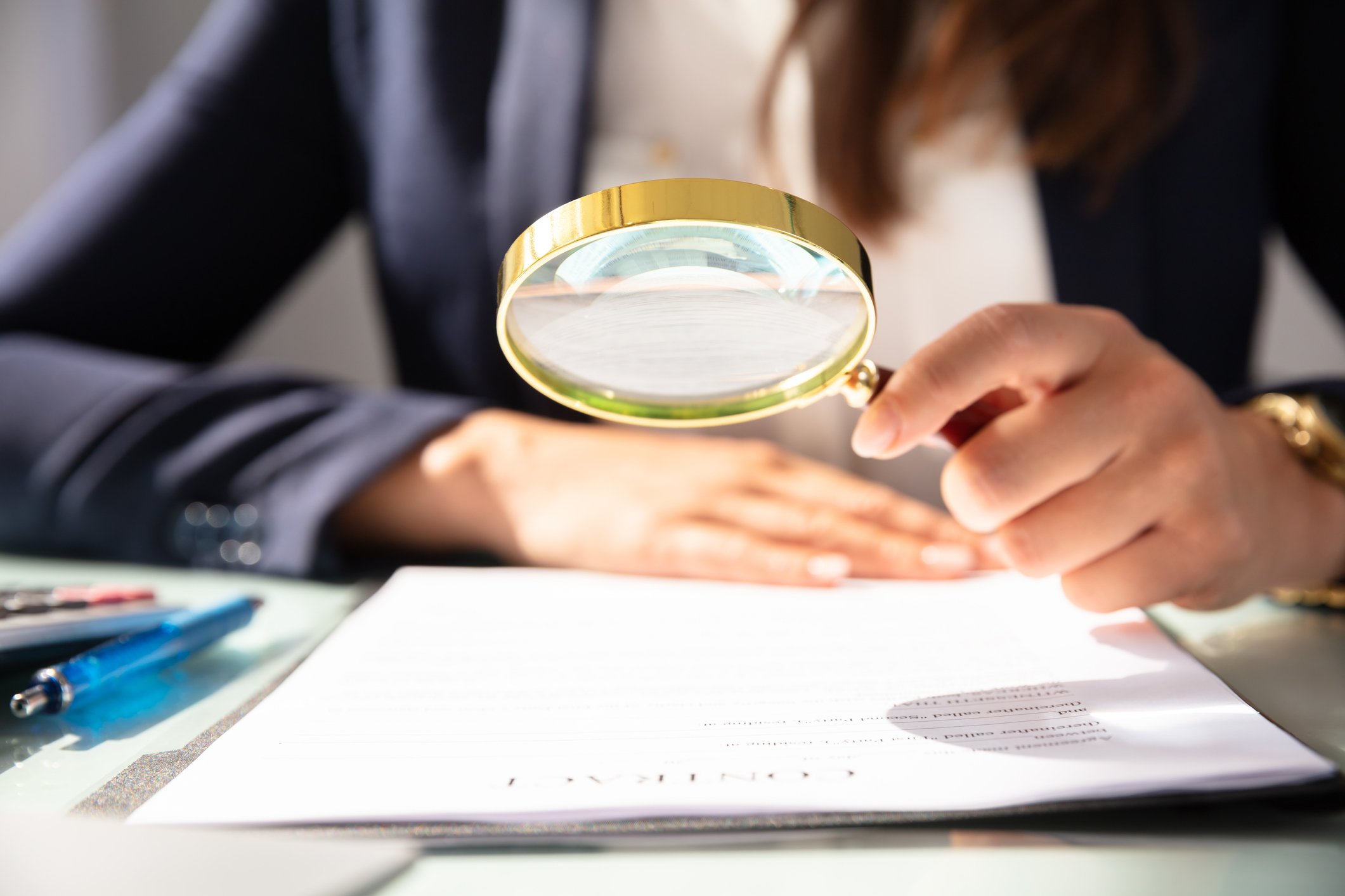 closeup of a magnifying glass held by a woman inspecting a document. 