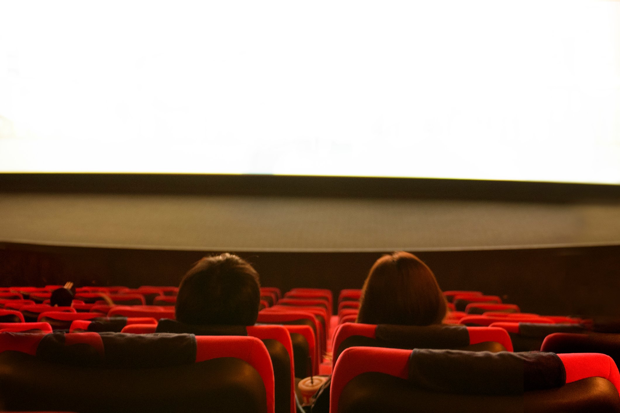 Two people sitting in a movie theater looking at the screen.