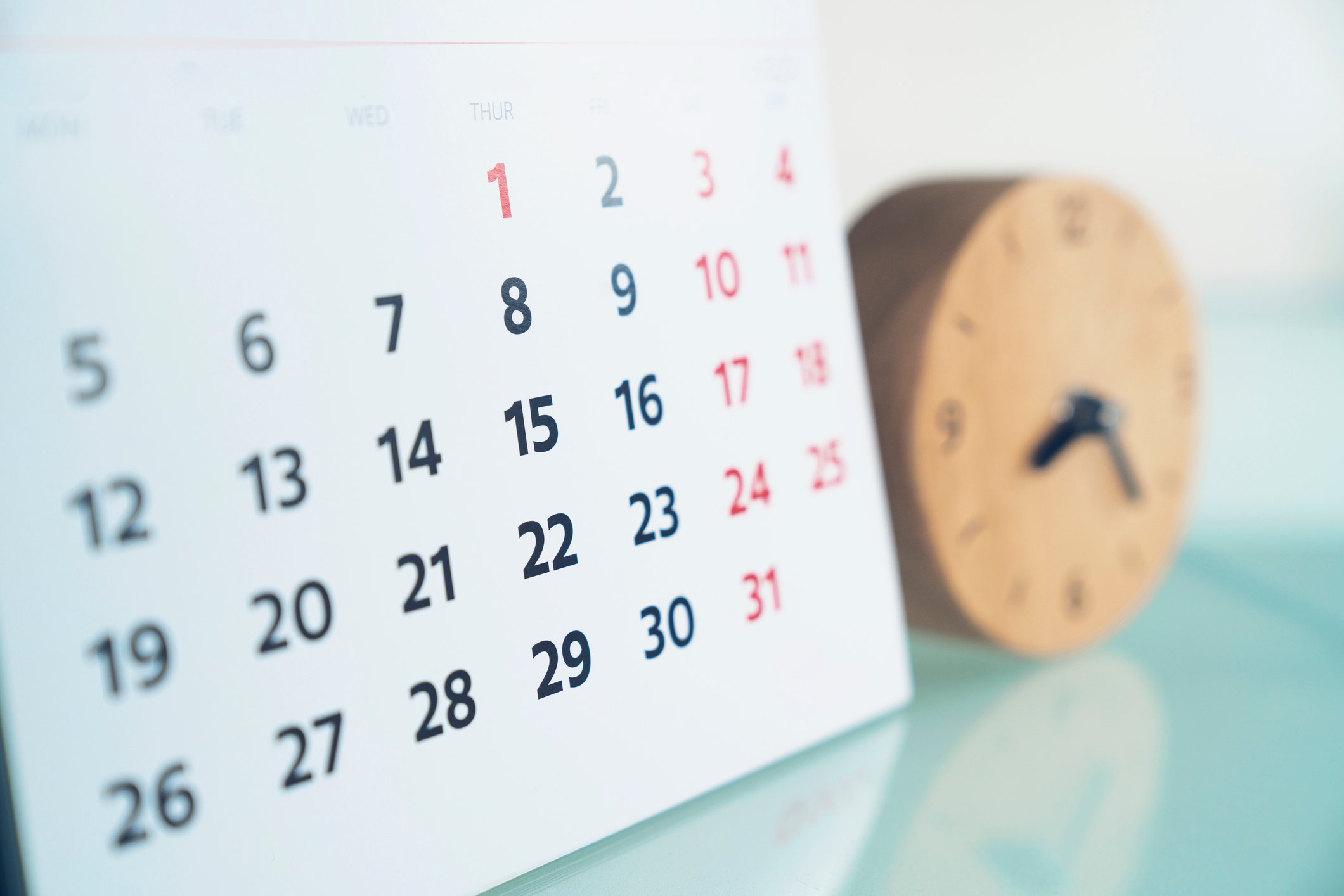 A calendar and an out-of-focus clock on a table.