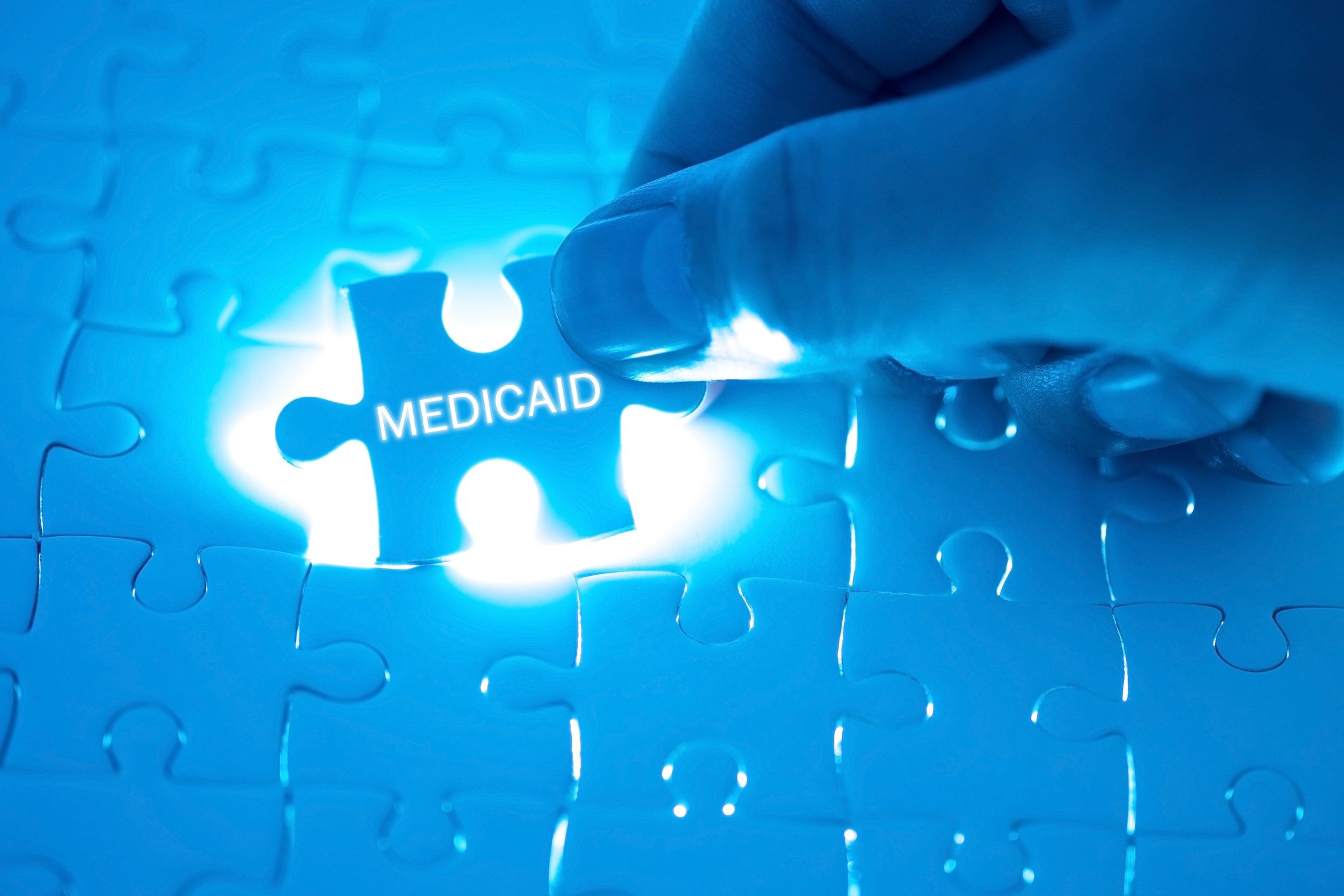 Hand holding jigsaw puzzle piece with Medicaid printed on it