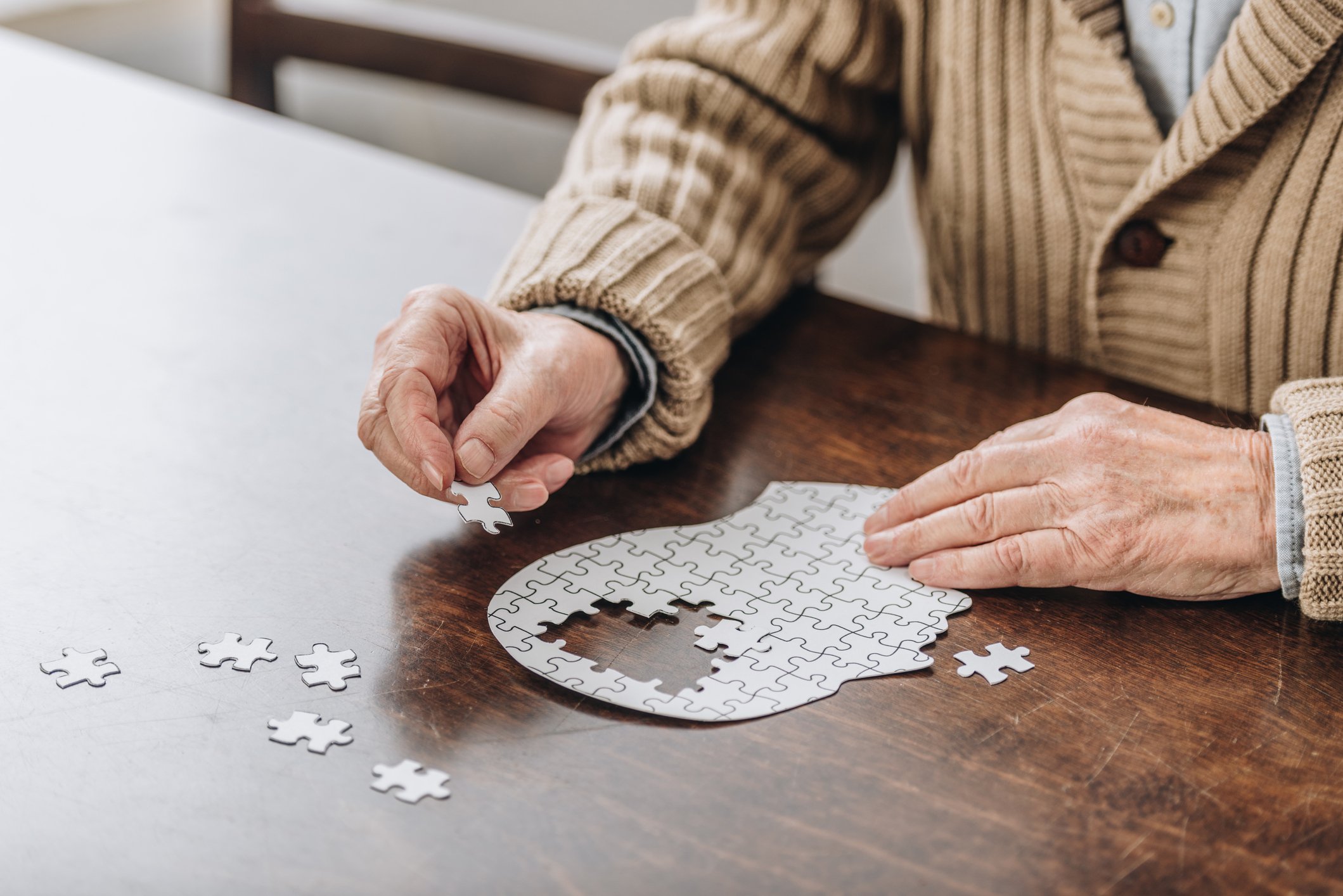 An elderly person assembling a puzzle of a human head at a wooden table.
