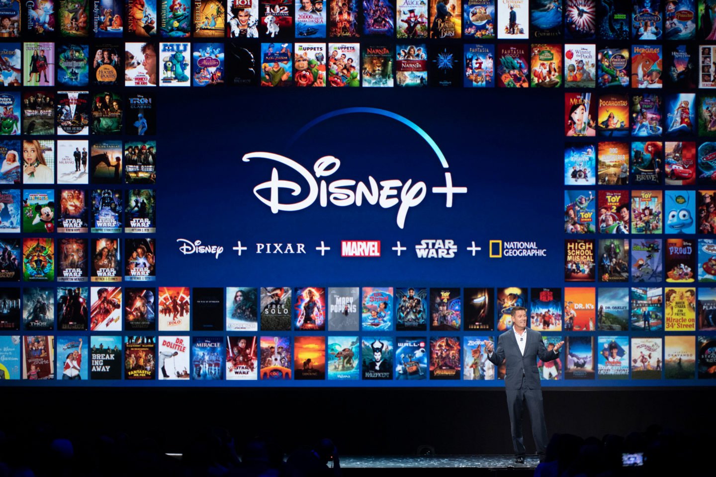 A man standing in front of a screen displaying dozens of Disney+ titles.