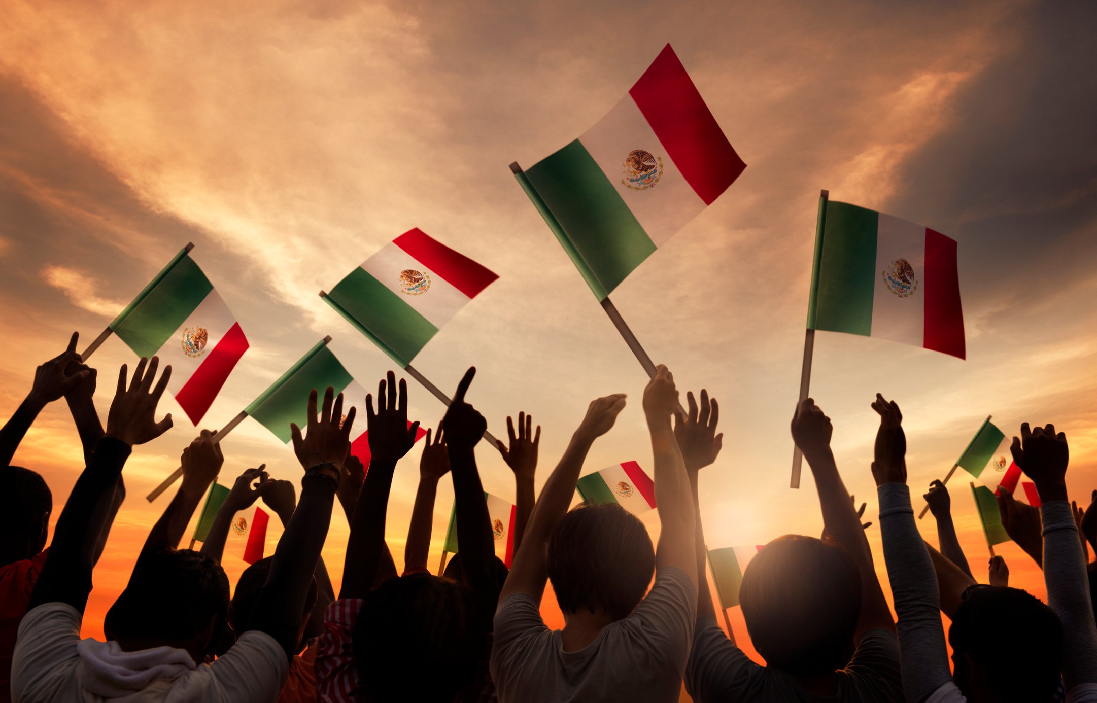 A group of people holding Mexican flags with the sun rising in the background