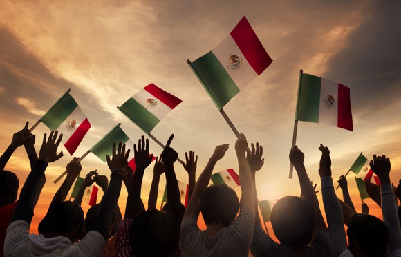 A group of people holding Mexican flags with the sun rising in the background
