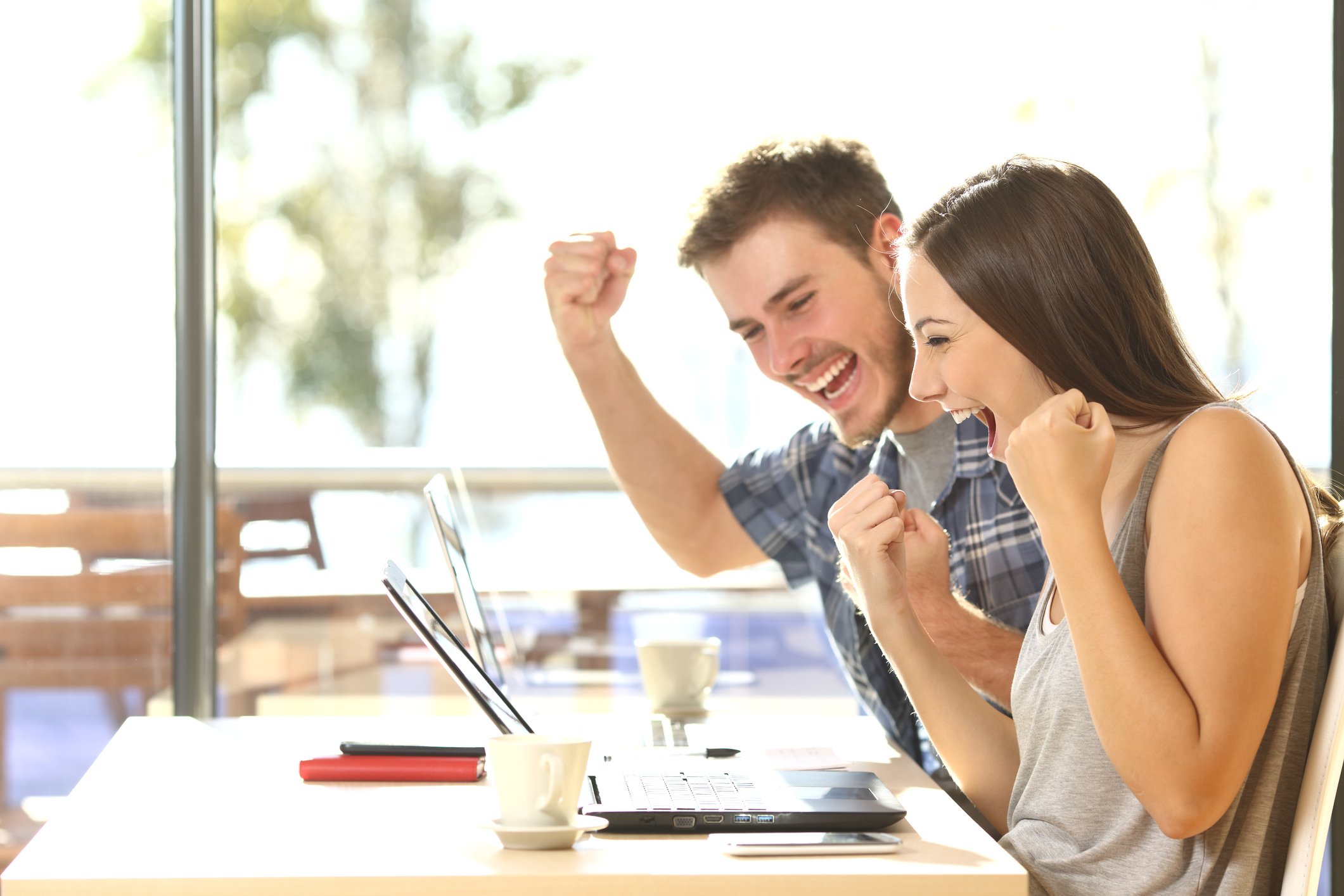 Young man and young woman smiling and holding clenched fists up while looking at a laptop screen