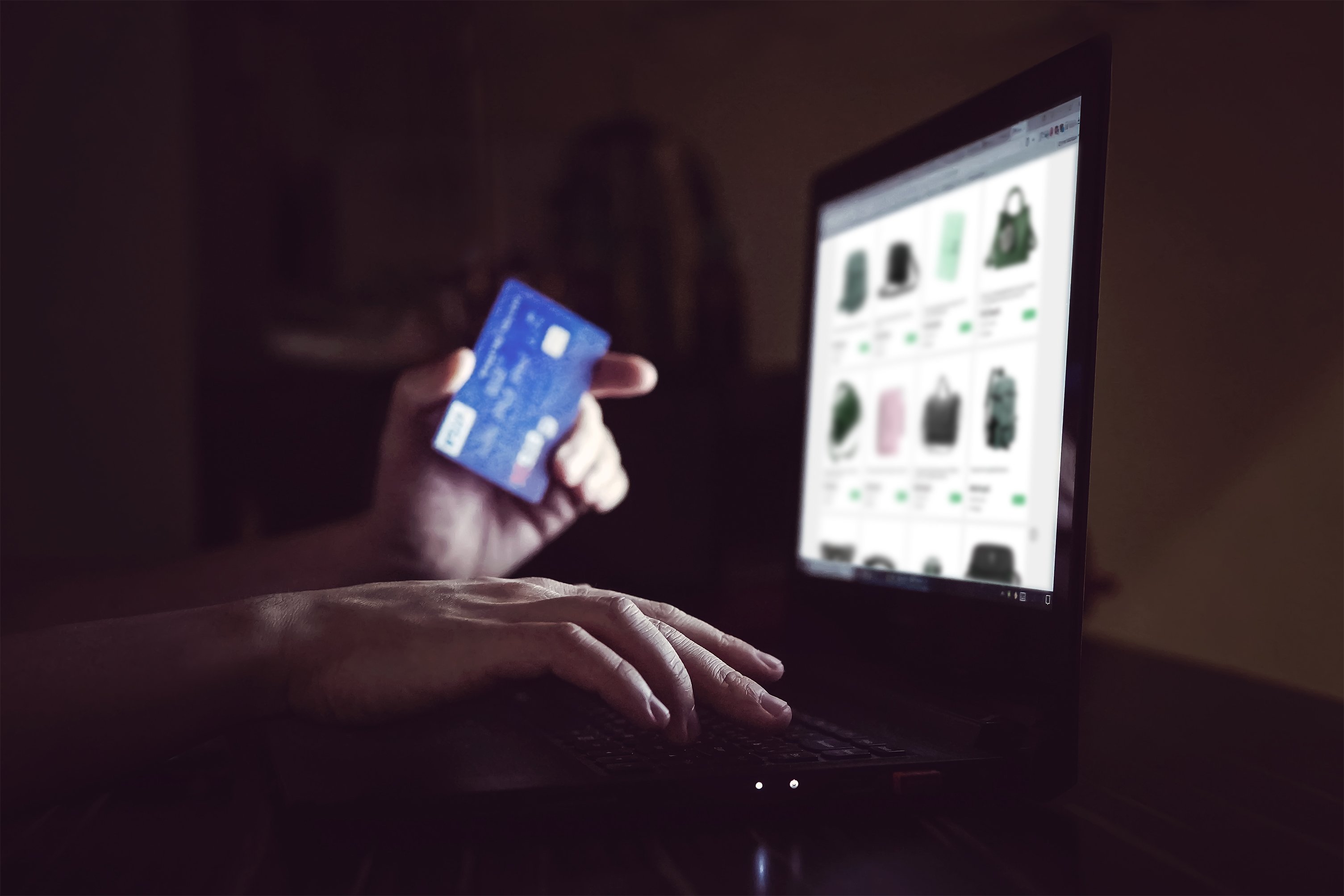 A person holds a credit cars near a computer in the dark.