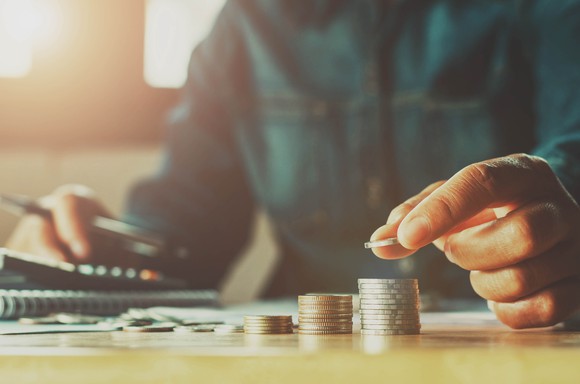 A hand putting a coin on a stack of coins.