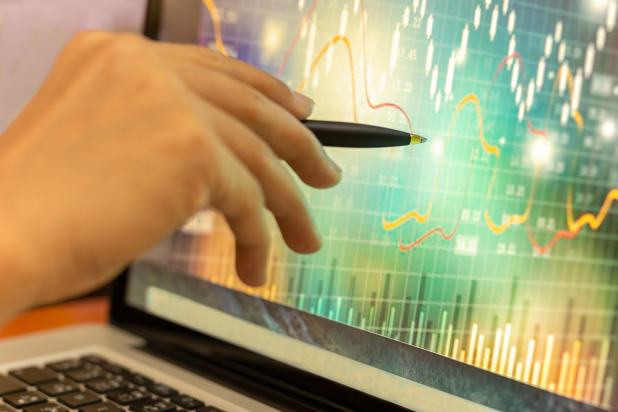 Hand holding pen pointing at stock graph displayed on a laptop screen