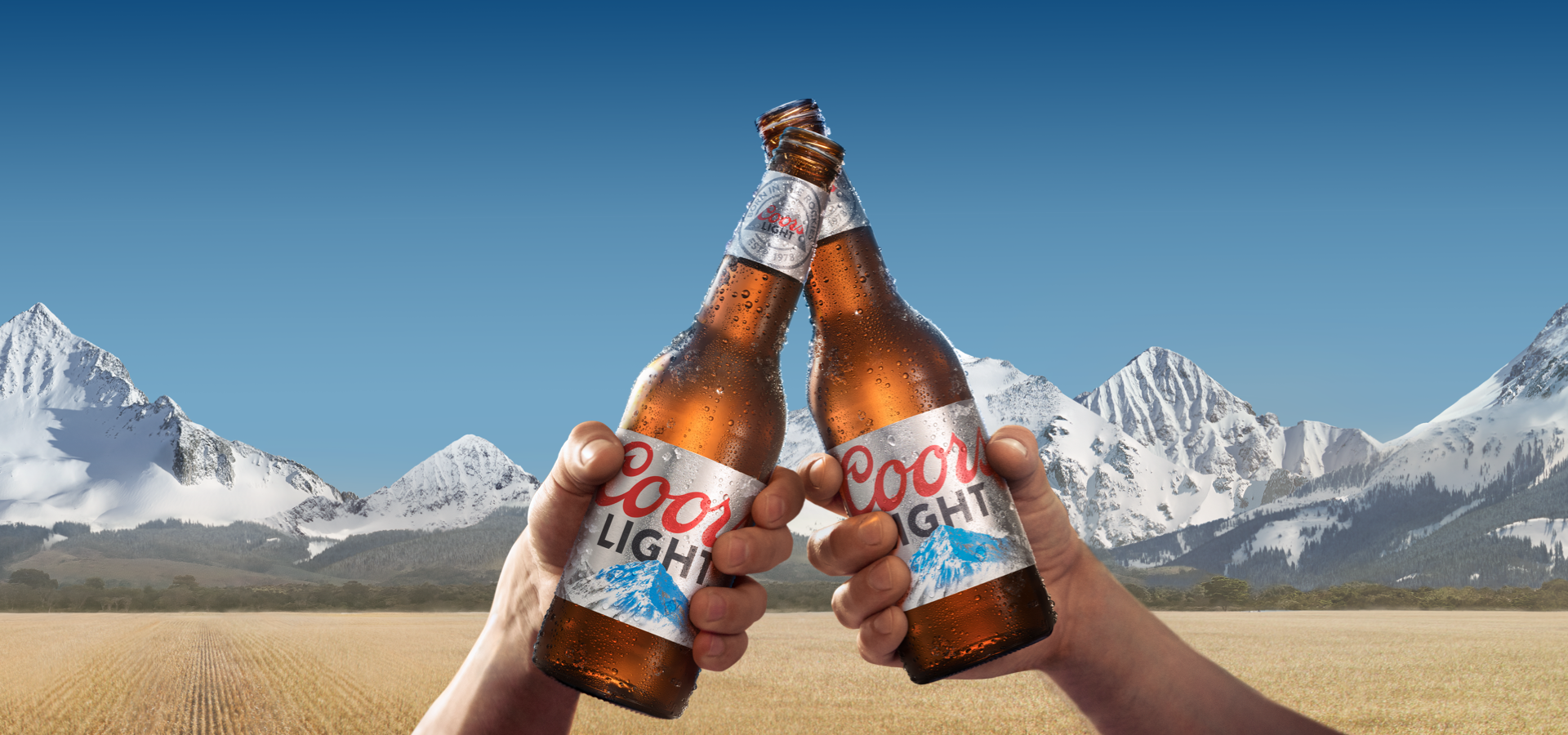 Two bottles of Coors Light in front of the Rocky Mountains.