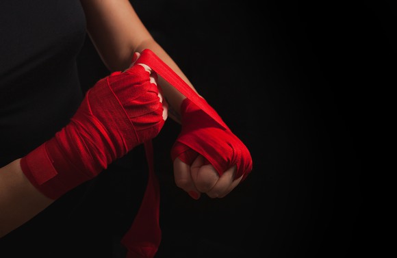 A fighter wrapping their hands in red boxer's straps.