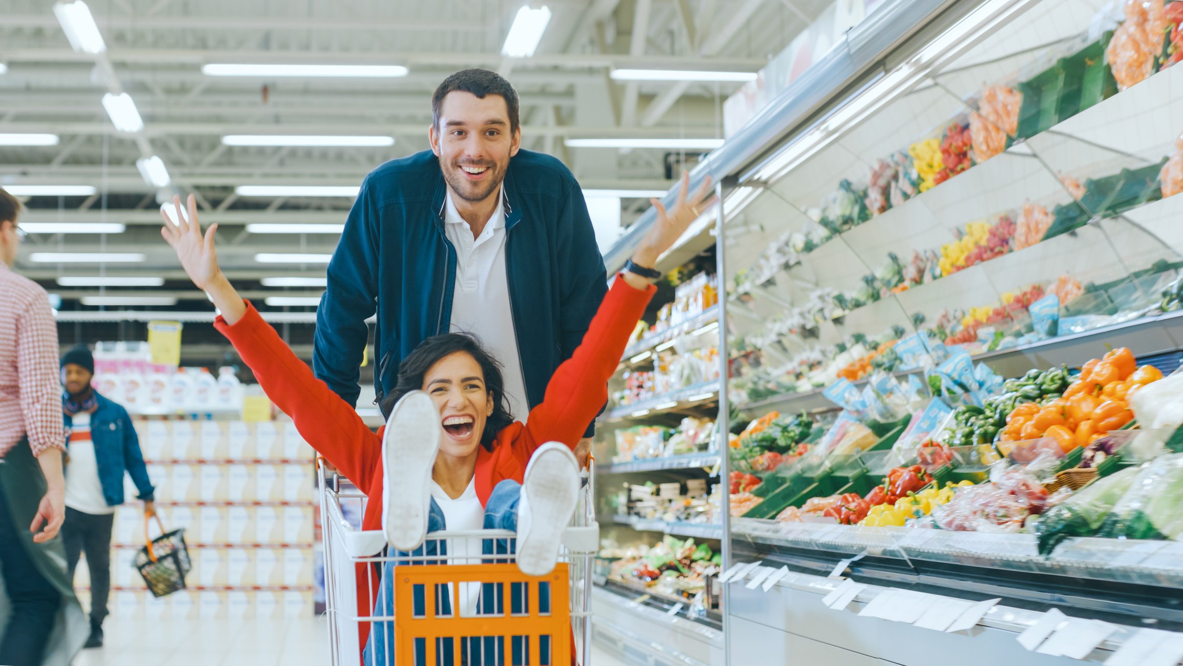 A man pushing an excited woman in a shopping cart through a grocery store