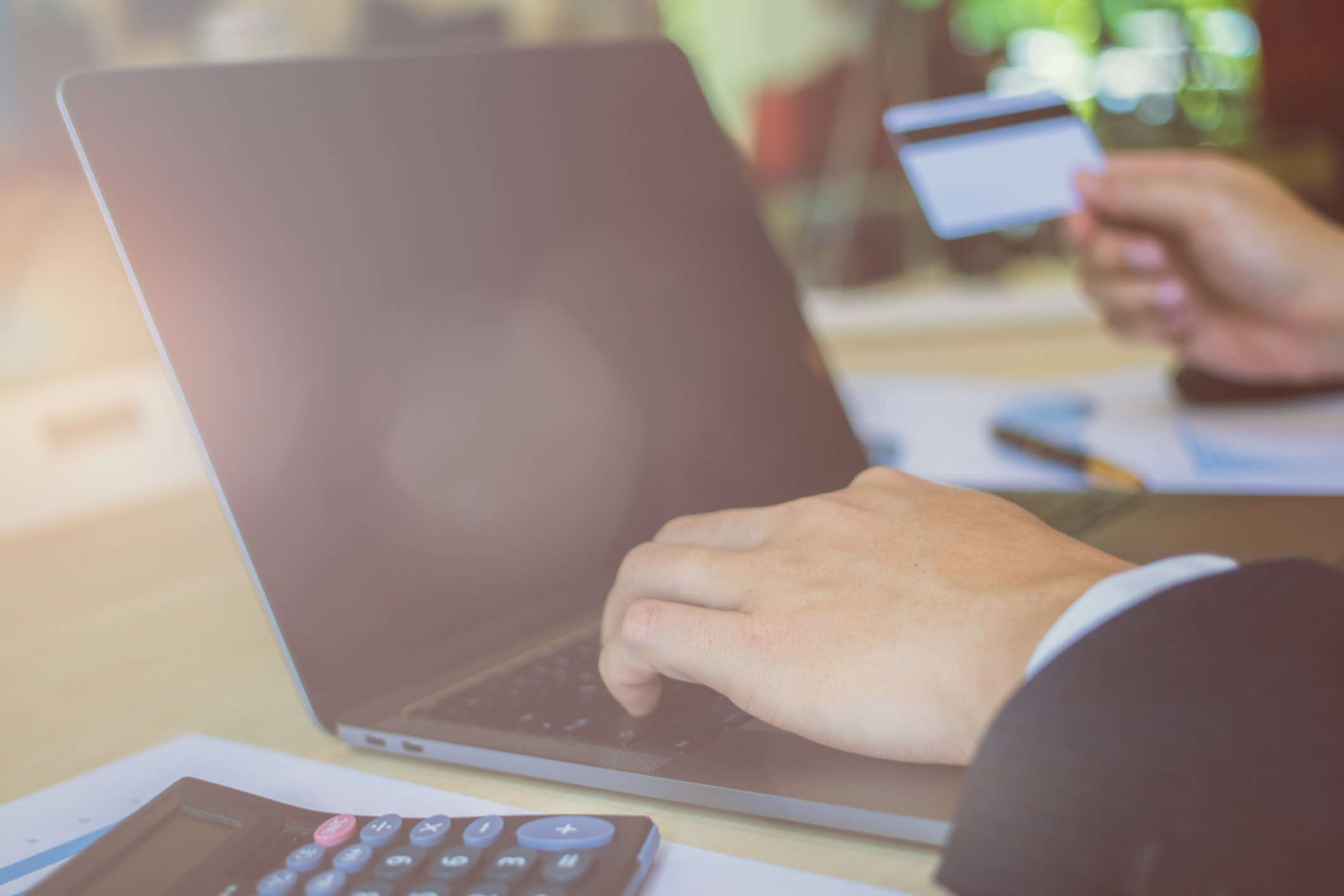 One hand touching a computer and making a payment, while the other hand holds a credit card.
