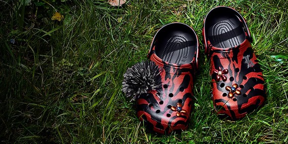 Red and black Crocs with a black kush ball on grass.