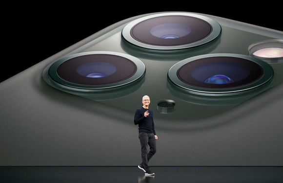 Tim Cook standing on stage in front of a closeup of the three camera system on the iPhone 11 Pro.