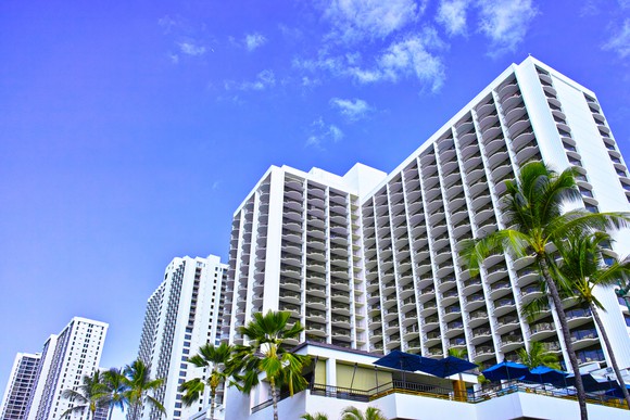 A multi-story hotel complex with white facade, flanked by palm trees.