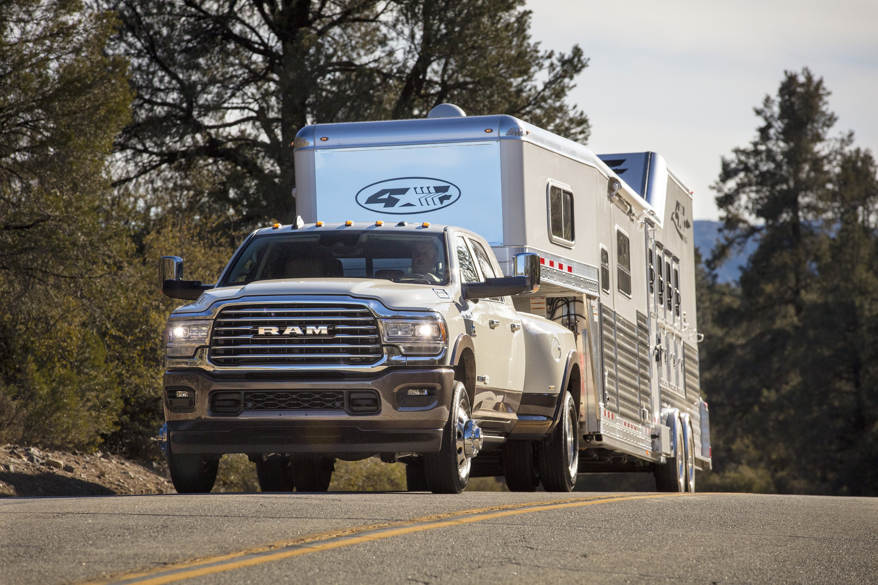 A 2019 Ram 3500 heavy-duty pickup is shown towing a horse trailer up a hill.