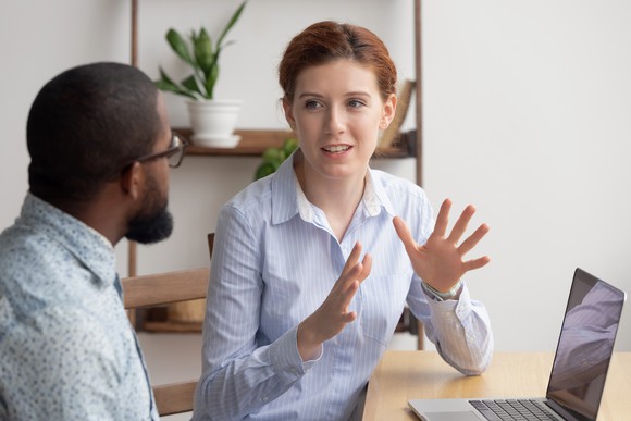 Two young co-workers in a business animatedly discuss a concept in a conference room.