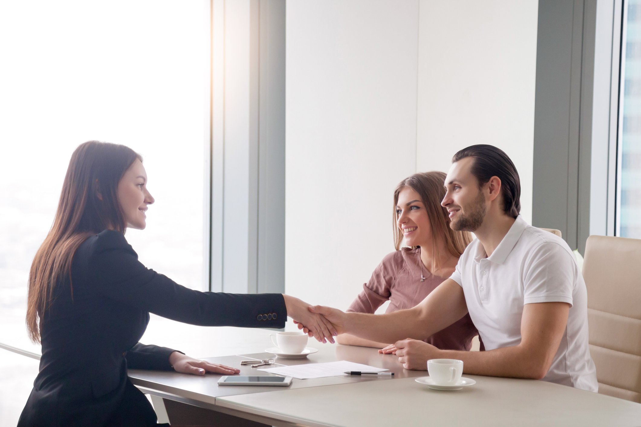 A young couple shakes hands with a banker after signing loan documents.