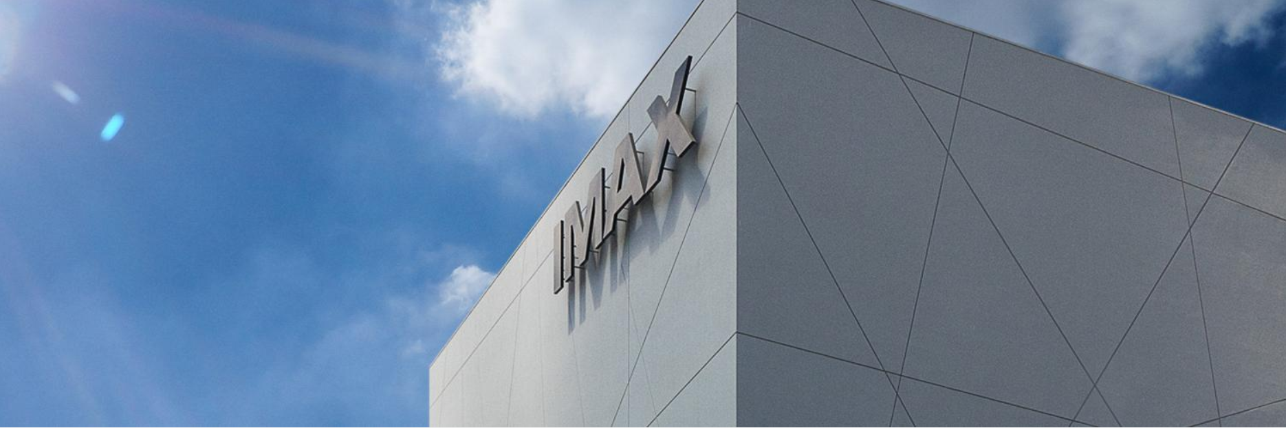 The IMAX logo at the top of a building against a brilliant blue sky.