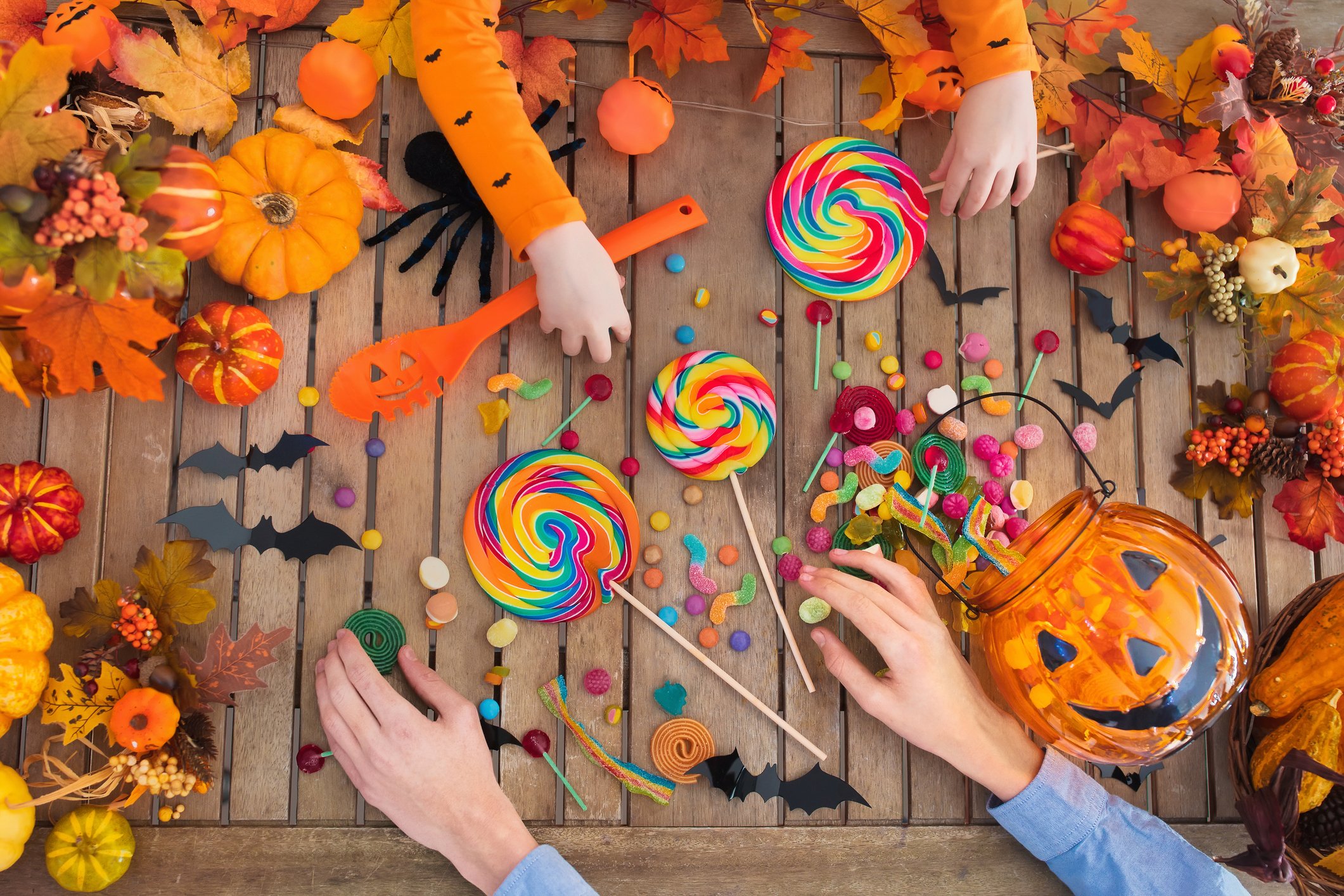 Hands grabbing Halloween candy from a table covered with Halloween decorations.