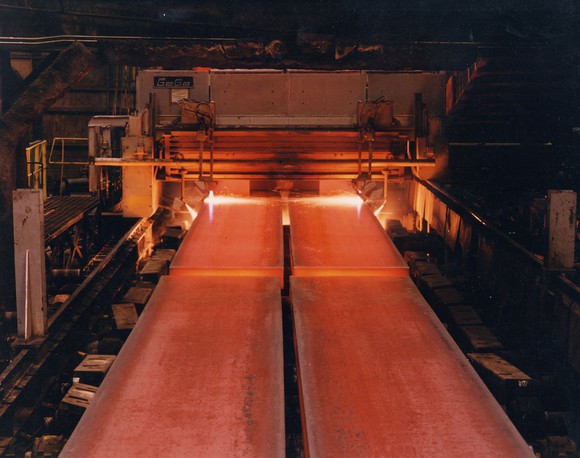 Two rows of red-glowing steel coming out of a furnace on a conveyor belt.