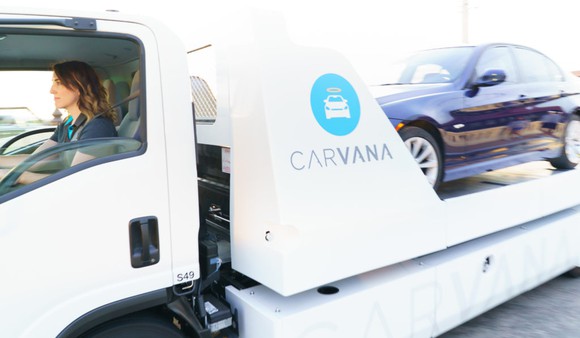 A Carvana employee drives a truck loaded with a vehicle to make a delivery to a customer.