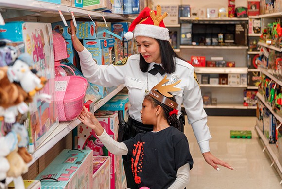 Adult female with Santa hat helping child with reindeer ears choose a toy from Target shelves.