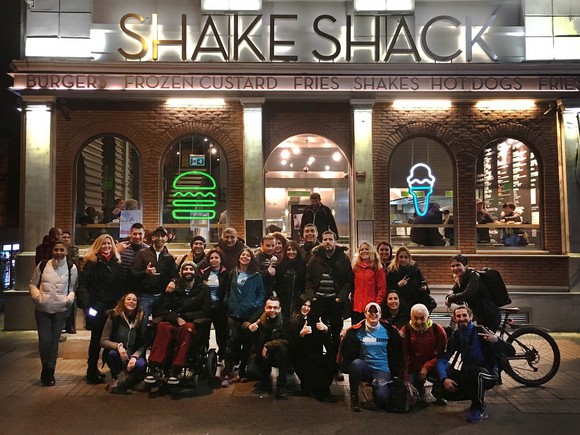 Shake Shack store with about two dozen people standing or sitting outside it.