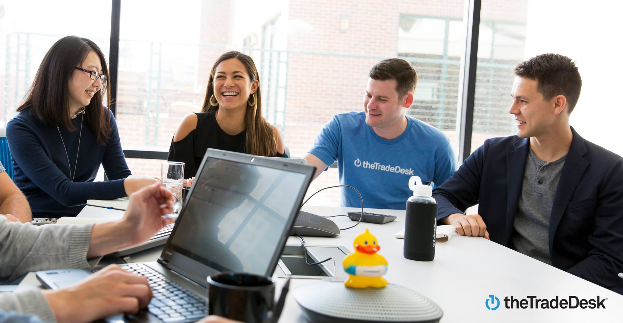 A group of people sitting around a table, with one wearing a t-shirt with The Trade Desk logo.