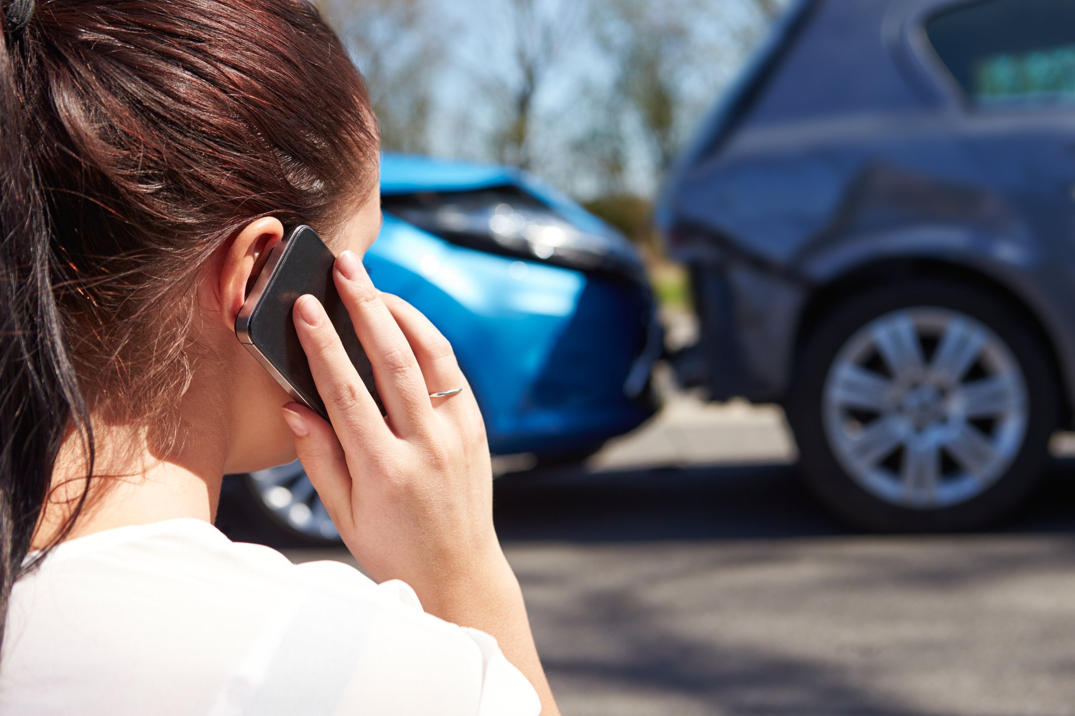 A woman making a call on her smartphone while standing in front of two cars involved in an accident.
