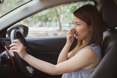 Young woman in car holding nose
