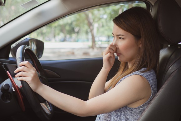 Young woman in the driver's seat of a car, holding her nose.