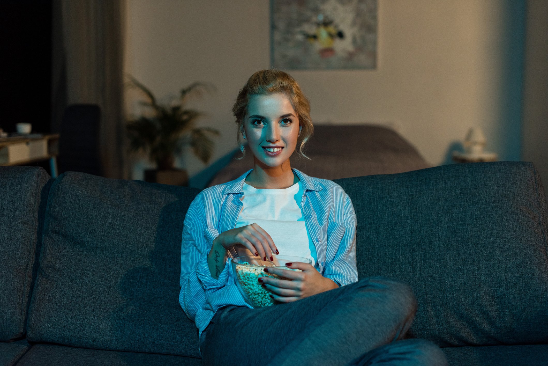 A young woman eating popcorn and watching TV in her living room.