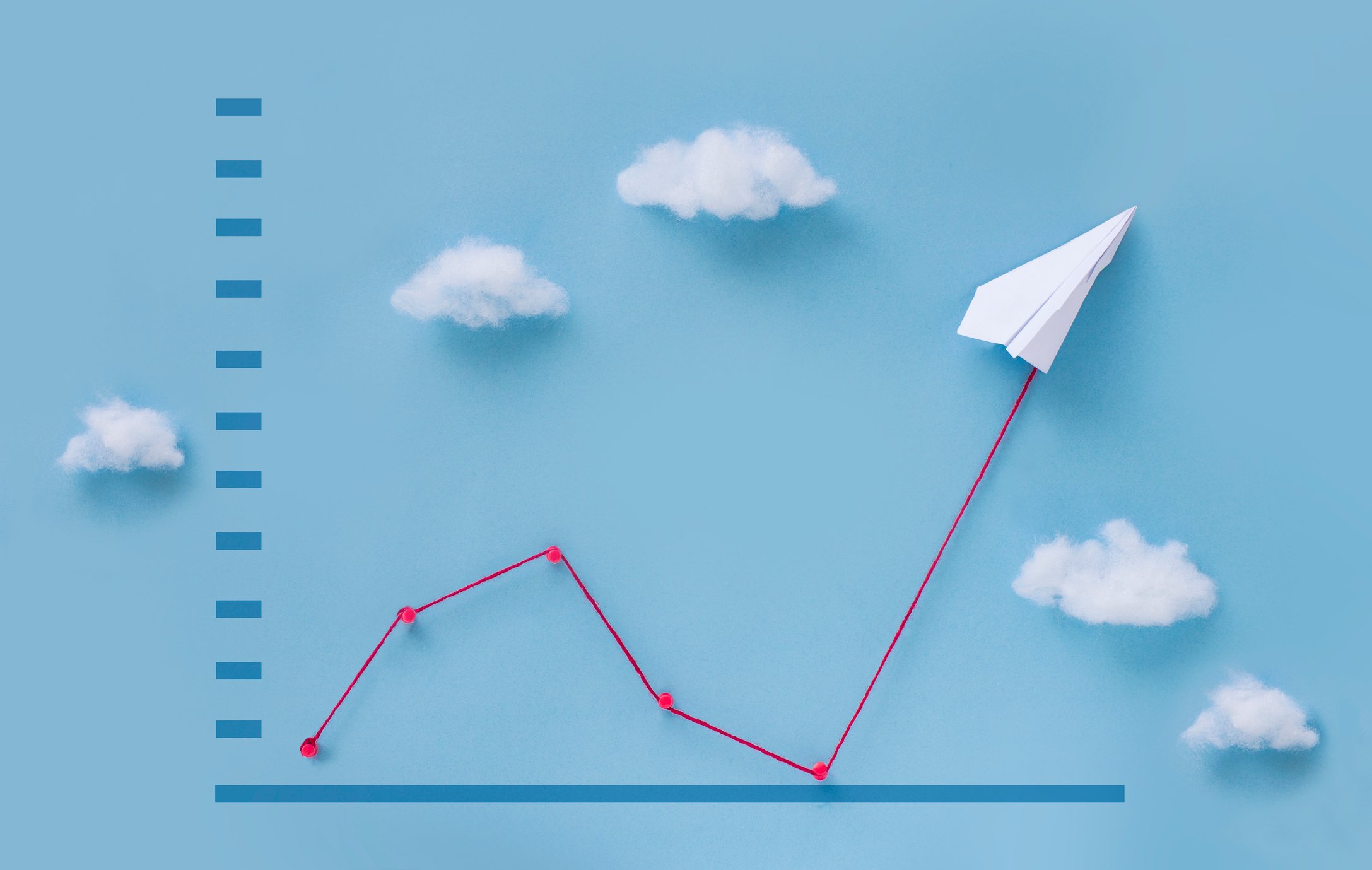 A paper plane pulling up a red zigzag line upward on a chart.