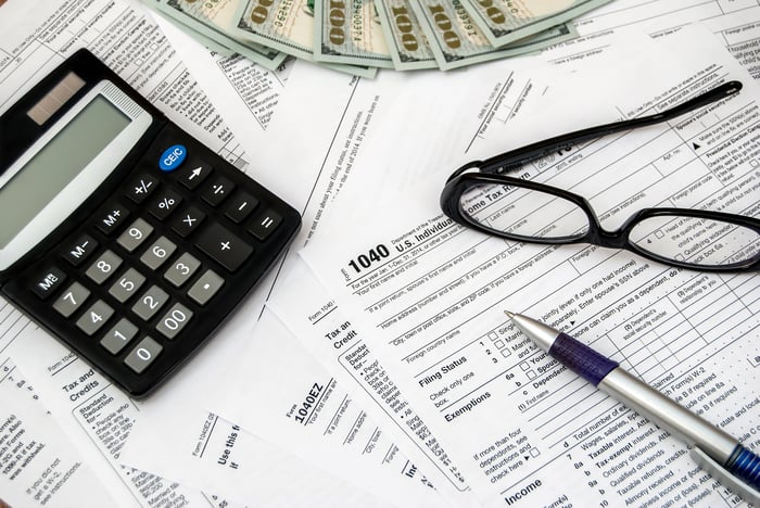 Tax forms, calculator, glasses, pen, and cash on a table.