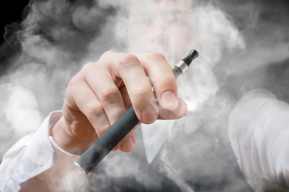 Man holding a vaping device with smoke surrounding him.