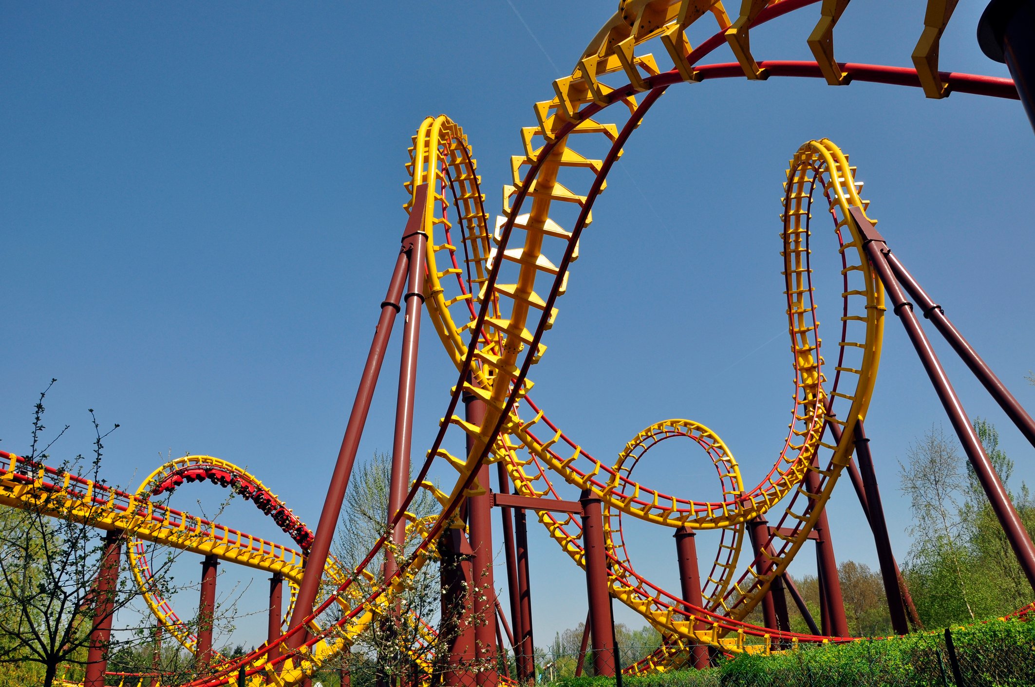 Close-up shot of an intricate roller coaster, showing lots of twists and loops in red and yellow steel tubing against a clear blue sky.