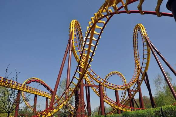 Close-up shot of an intricate roller coaster, showing lots of twists and loops in red and yellow steel tubing against a clear blue sky.