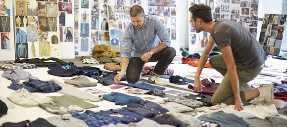 Two designers with clothing laid out on the floor in front of them.
